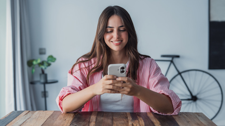 Smiling woman sitting on a couch looks down at smartphone in her hands