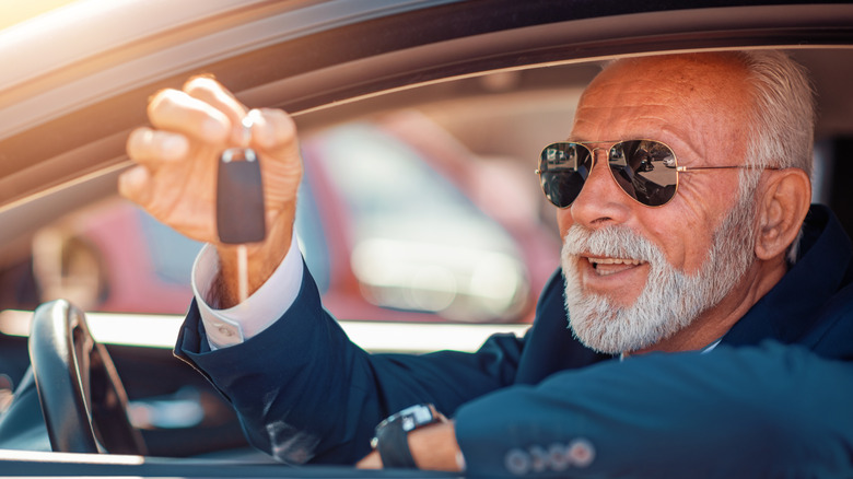 A senior-aged man sitting in the driver seat while holding the keys to a new car