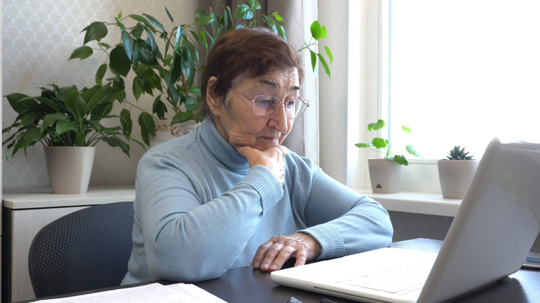 A retirement-aged woman reviewing some documents on her laptop