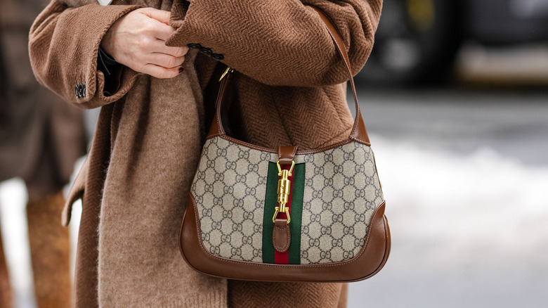 Close up of woman wearing thick winter coat, holding Gucci Jackie 1961 handbag