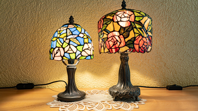 A pair of Tiffany stained glass lamps, turned on, placed on a doily