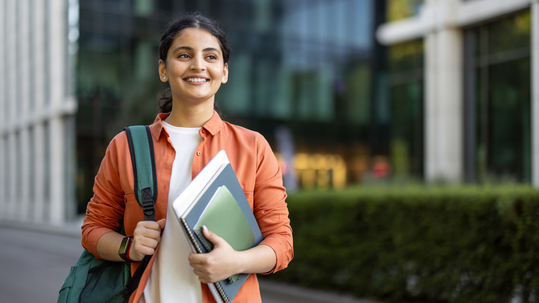 A smilling, colleg-aged woman wearing a backpack and holding notebooks