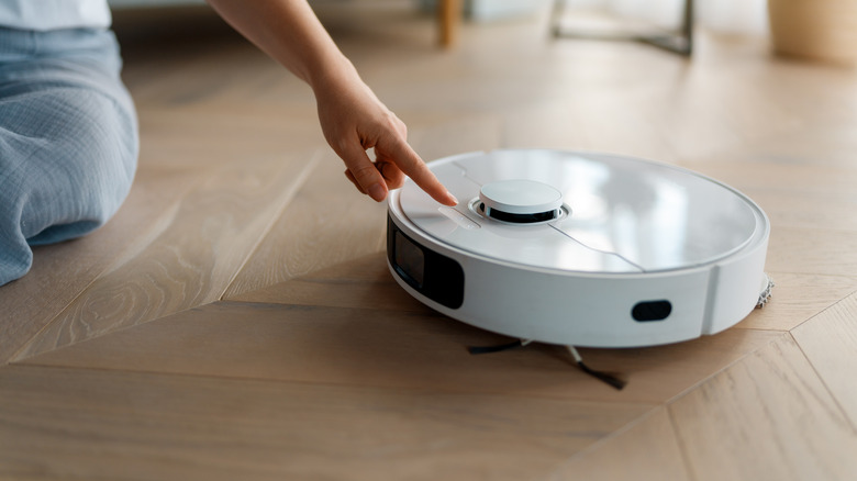A woman's hand reaching to press a button on a robot vacuum