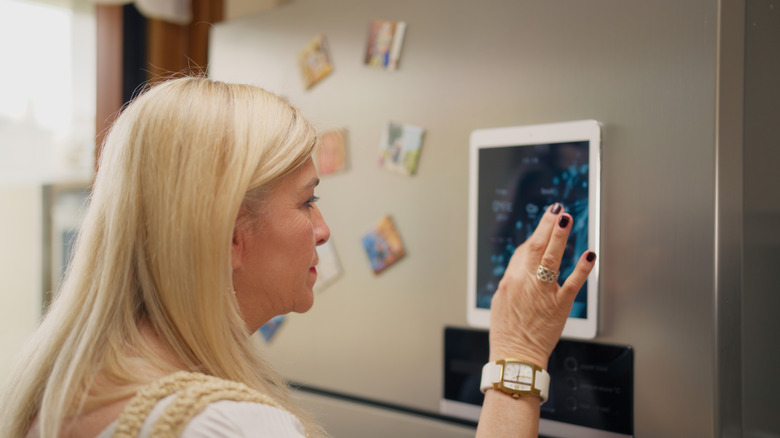Older woman touching touch screen on smart refrigerator