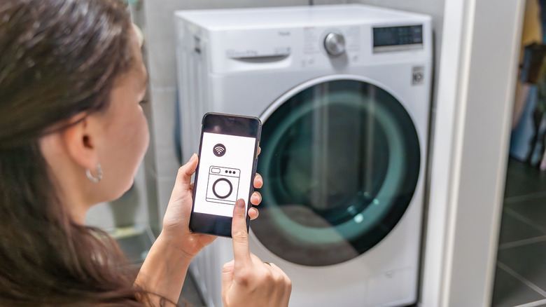 A young woman operates a smart washing machine using an app on her phone