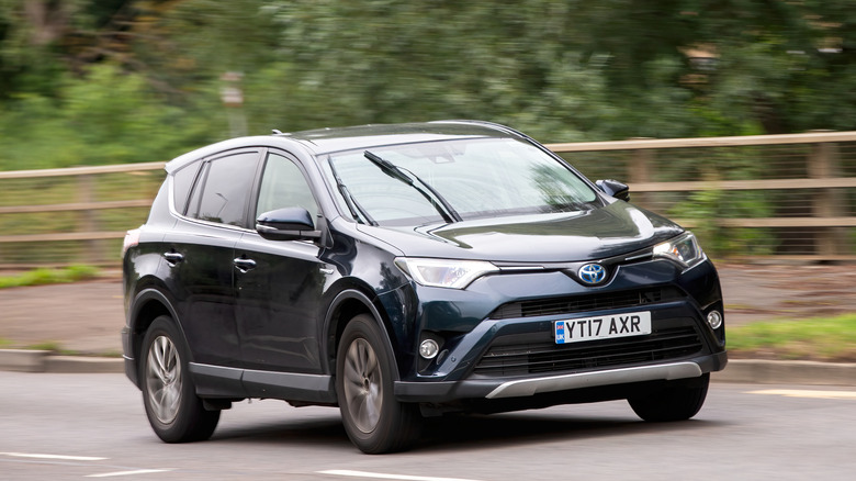 A black Toyota Rav4 hybrid electric SUV car driving on a British road.