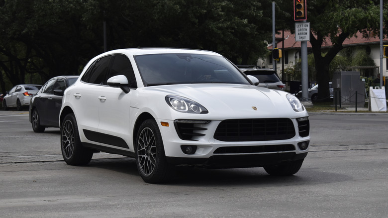 A white Porsche Macan SUV cruising in a downtown district.