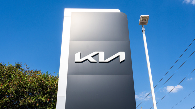A sign for a Kia Dealership next to a lamppost against a blue sky