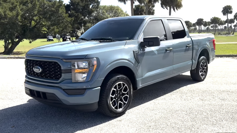 A blue 2023 Ford F-150 SuperCrew XL parked in front of a field lined with palm trees on a sunny day