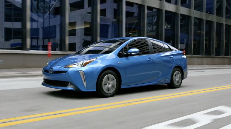 A blue 2021 Toyota Prius driving past a building with large windows