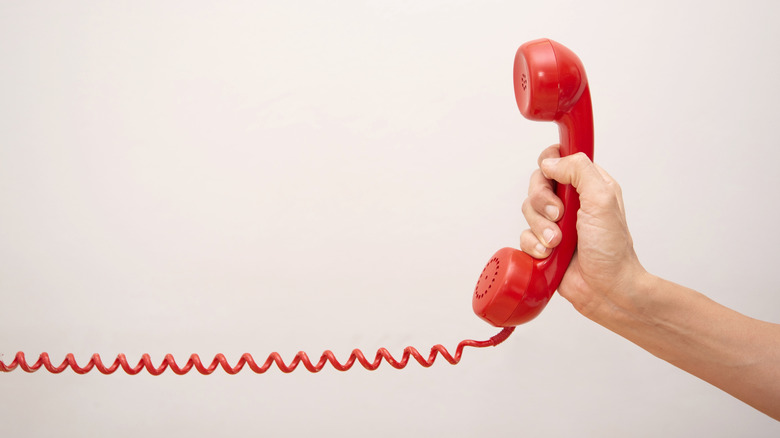 An old red landline phone reciever with a coiled phone cord
