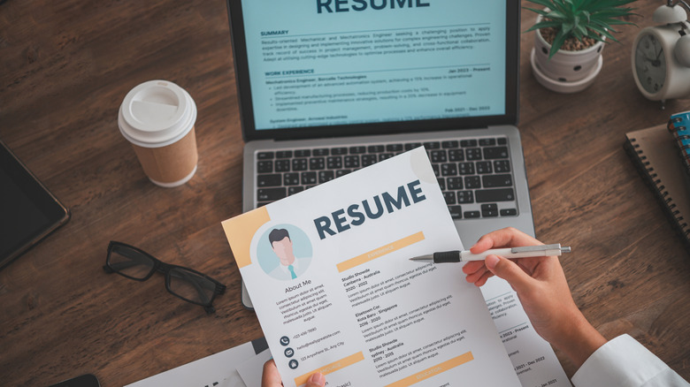 First-person perspective of someone comparing a resume in front of a laptop with another resume on the screen.