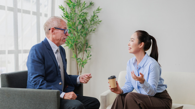 An older man having coffee with a younger female coworker in an office.