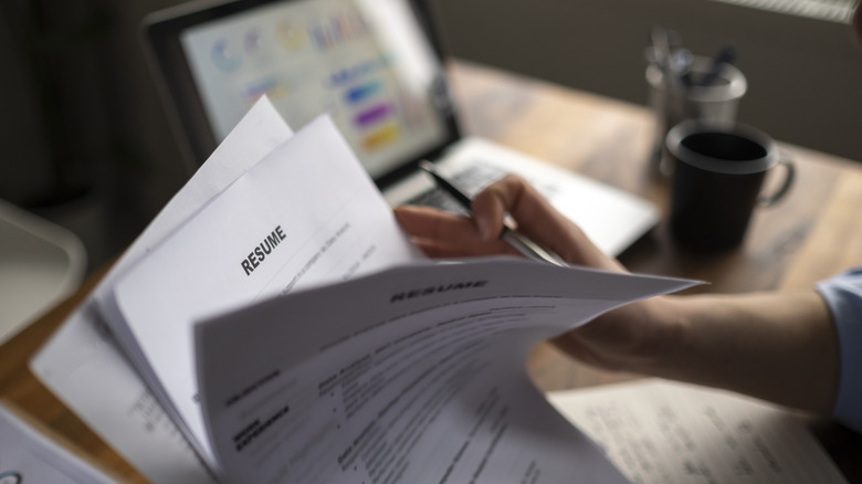 Man holding pen flips through a stack of resumes