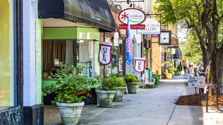 Pedestrians walk down a sidewalk lined with colorful stores and potted plants in Shelby, North Carolina