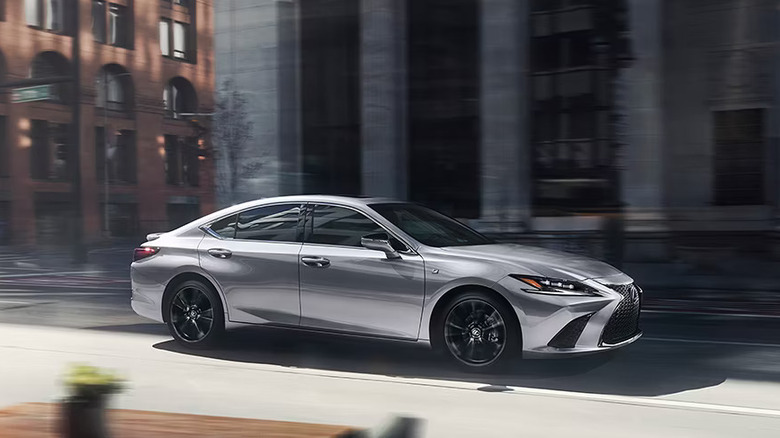 silver 2025 Lexus ES Hybrid rolling through city street in front of gray block building