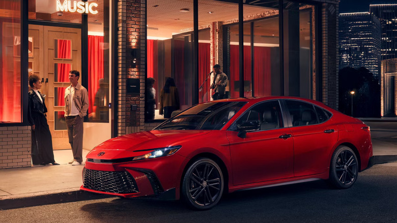 red 2026 Toyota Camry Hybrid parked at night on the street in front of music venue