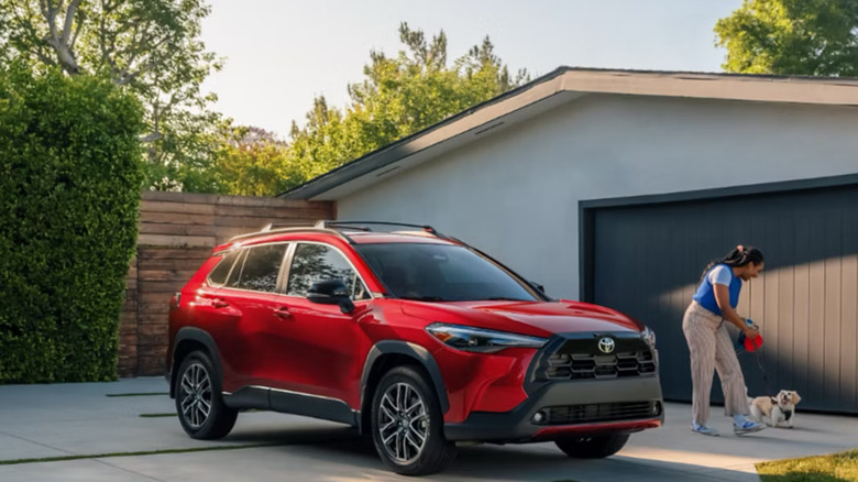 red 2026 Toyota Cross parked in driveway as woman walks dog in background