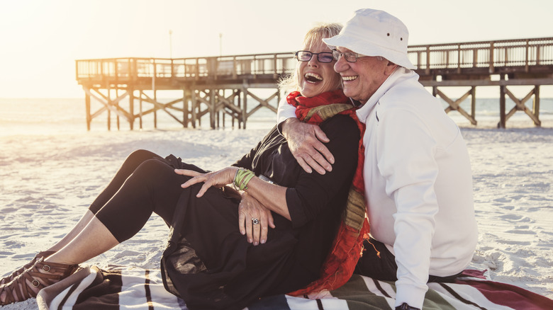 A laughing couple embracing on a beach at sundown with a pier in the background.