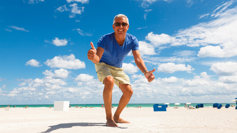 A mature man enjoying the beach and giving two thumbs up.