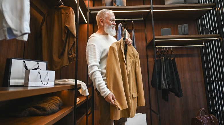 A mature man smiling while holding a blazer in walk-in closet.