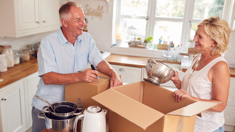 A mature couple placing items into boxes in their kitchen to downsize.