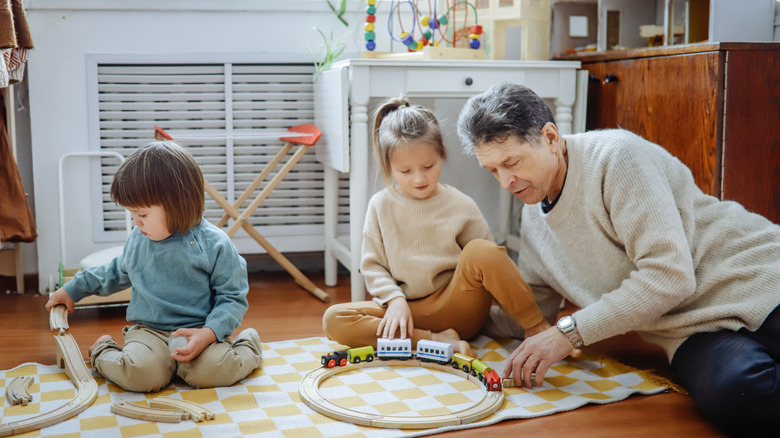 A grandad playing with toy trains with his two young grandchildren.