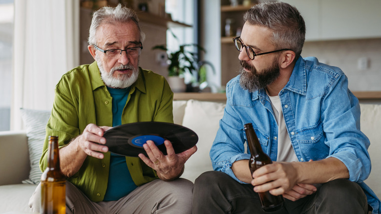 A senior man holding a record talking to a Gen X man having a beer.