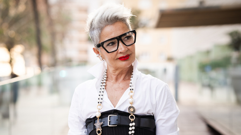 A senior woman in a funky outfit wearing a large pearl necklace.