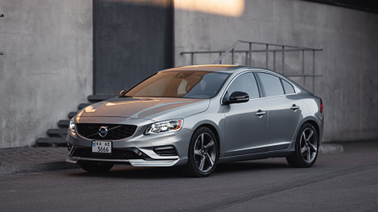 Thee quarter front view of sporty Volvo S60 parked in a city near concrete wall and fire escape exit.