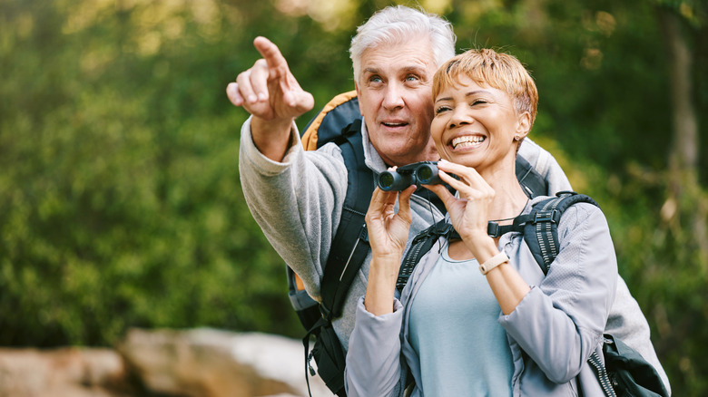 senior couple outside smiling and pointing with binoculars