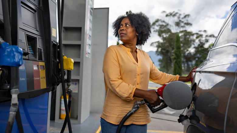 An older woman looking perplexed at the gas pump while filling up her tank