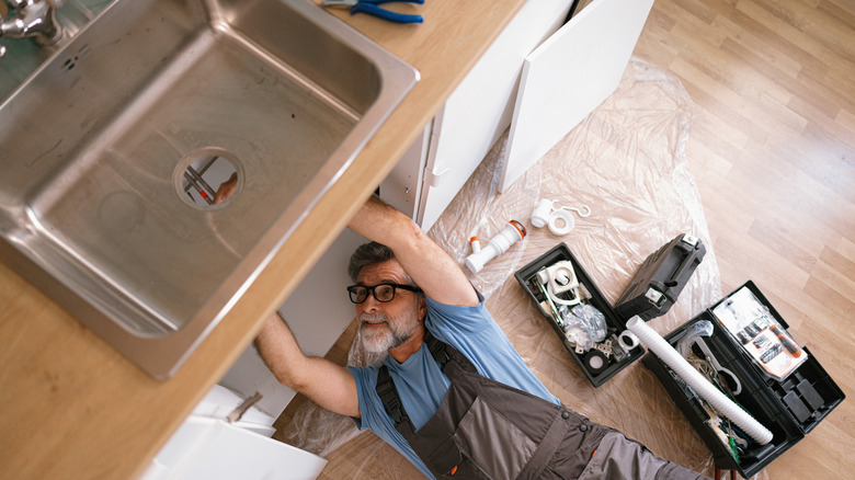Top view of a plumber fixing the sink in the kitchen.