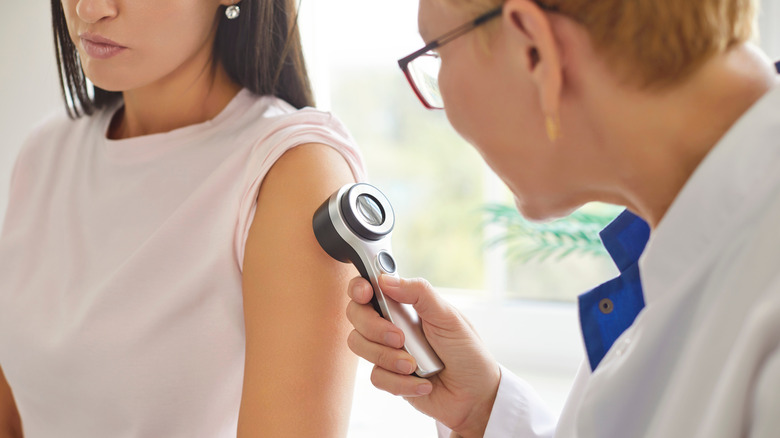In dermatology clinic healthcare professional examining patient skin with handheld device.