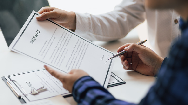 Man in office showing an insurance policy and pointing with a pen where the policyholder must to sign.