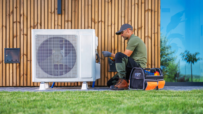 A technician servicing an air conditioning unit located beside a modern home.