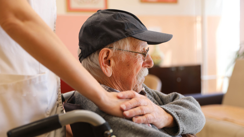 Elderly man in a wheelchair talking to a nurse at a nursing home.