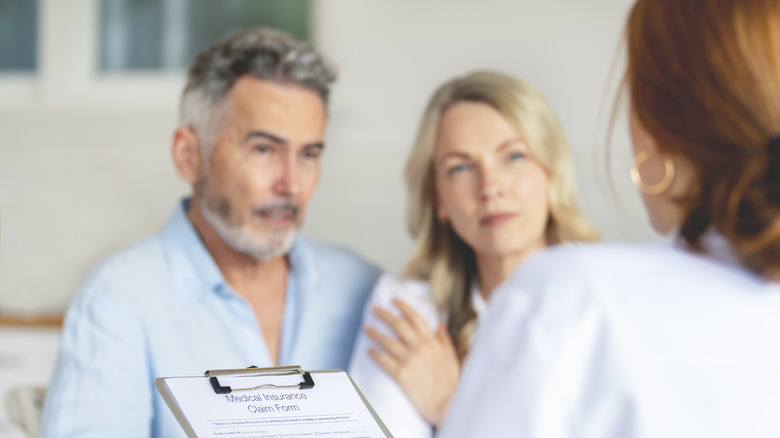 Doctor filling out medical insurance form with mature couple who look worried and upset