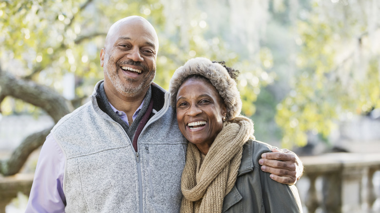 Senior couple, guitar and romance while laughing and singing a romantic or funny song to wife sitting on the sofa at home.