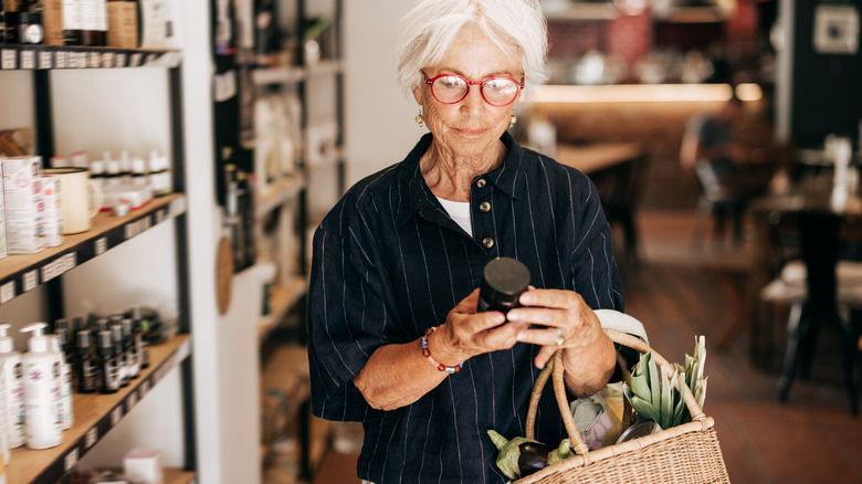 Mature woman with wicker handbag filled with vegetables examines small bottle