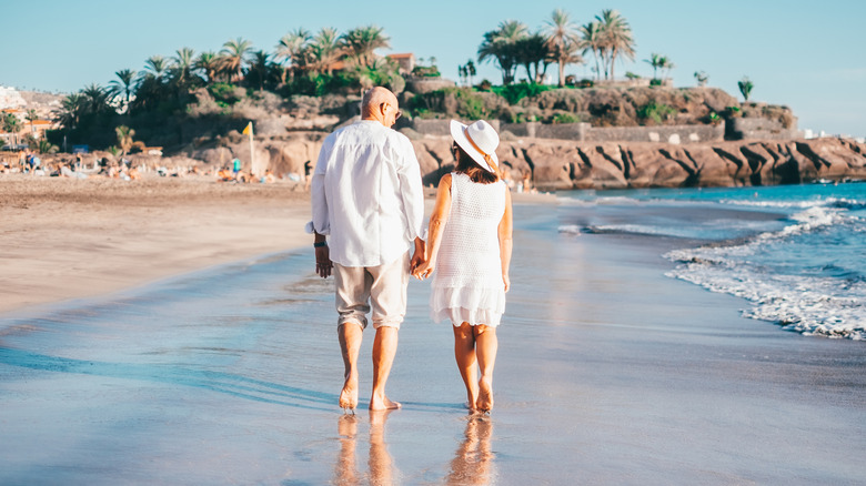 A couple of retired people walking on a beach in Spain