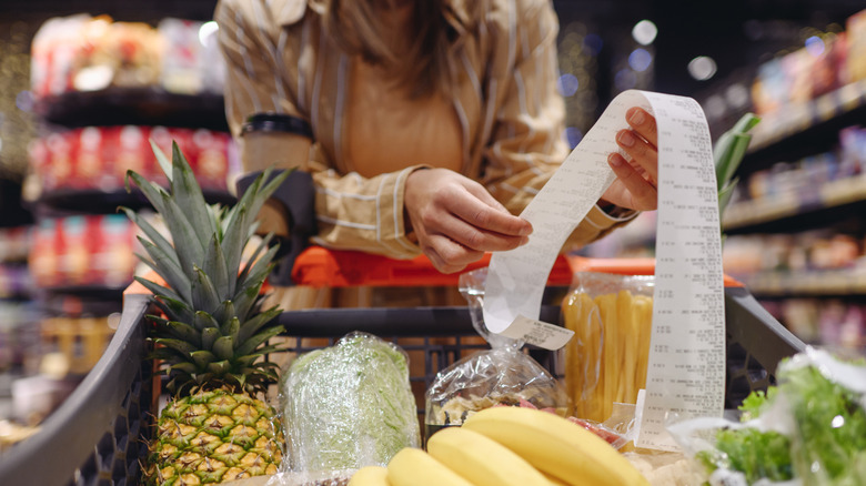 Person holding grocery receipt over cart.