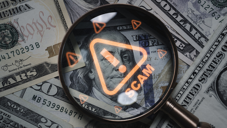 Magnifying glass focusing on scam warning symbol over dollar bills concept of financial fraud.