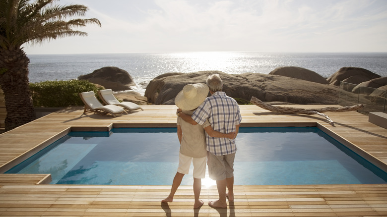 A senior couple on overlooking a pool next to the ocean at sunset.