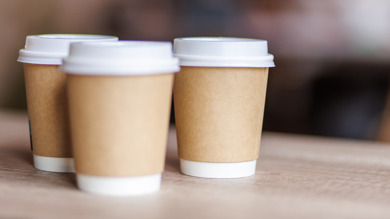 Three brown disposable coffee cups with white bases and lids on a desk
