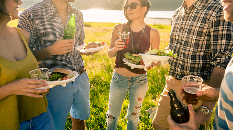 A group of young adults holding paper plates and drinks at a cookout