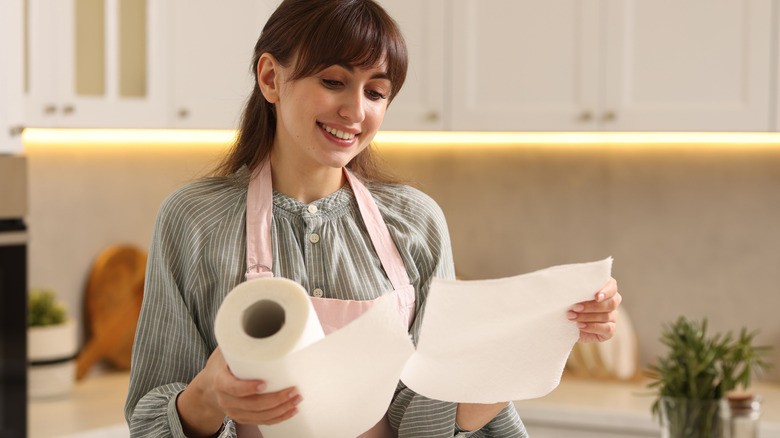 Woman smiling in kitchen, wearing an apron, while tearing paper towels