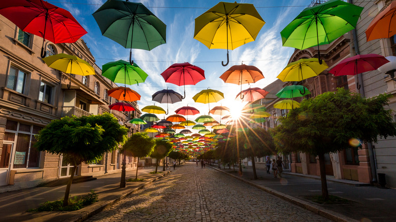 People walking under umbrellas hanging above cobblestone streets in Braila, Romania.