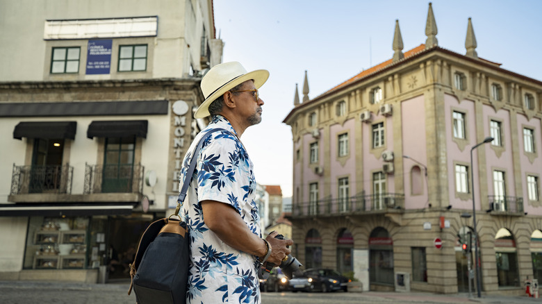 A mature man holding a camera walking the streets of Covilha, Portugal.