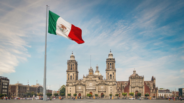 Mexican flag waves in breeze in front of historic buildings in Mexico City